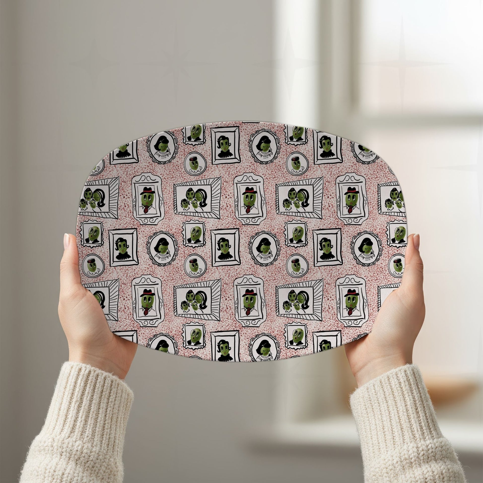 Two hands raising retro olive portrait serving platter in red colorway overhead showing full 10 by 14 inch oval gallery wall pattern in natural window light
