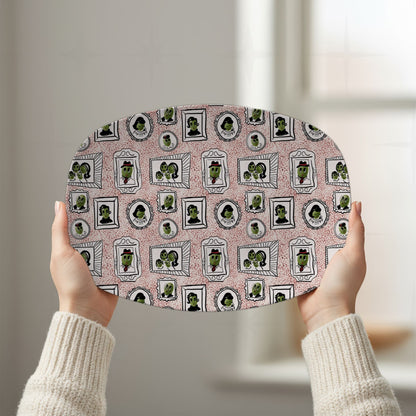 Two hands raising retro olive portrait serving platter in red colorway overhead showing full 10 by 14 inch oval gallery wall pattern in natural window light