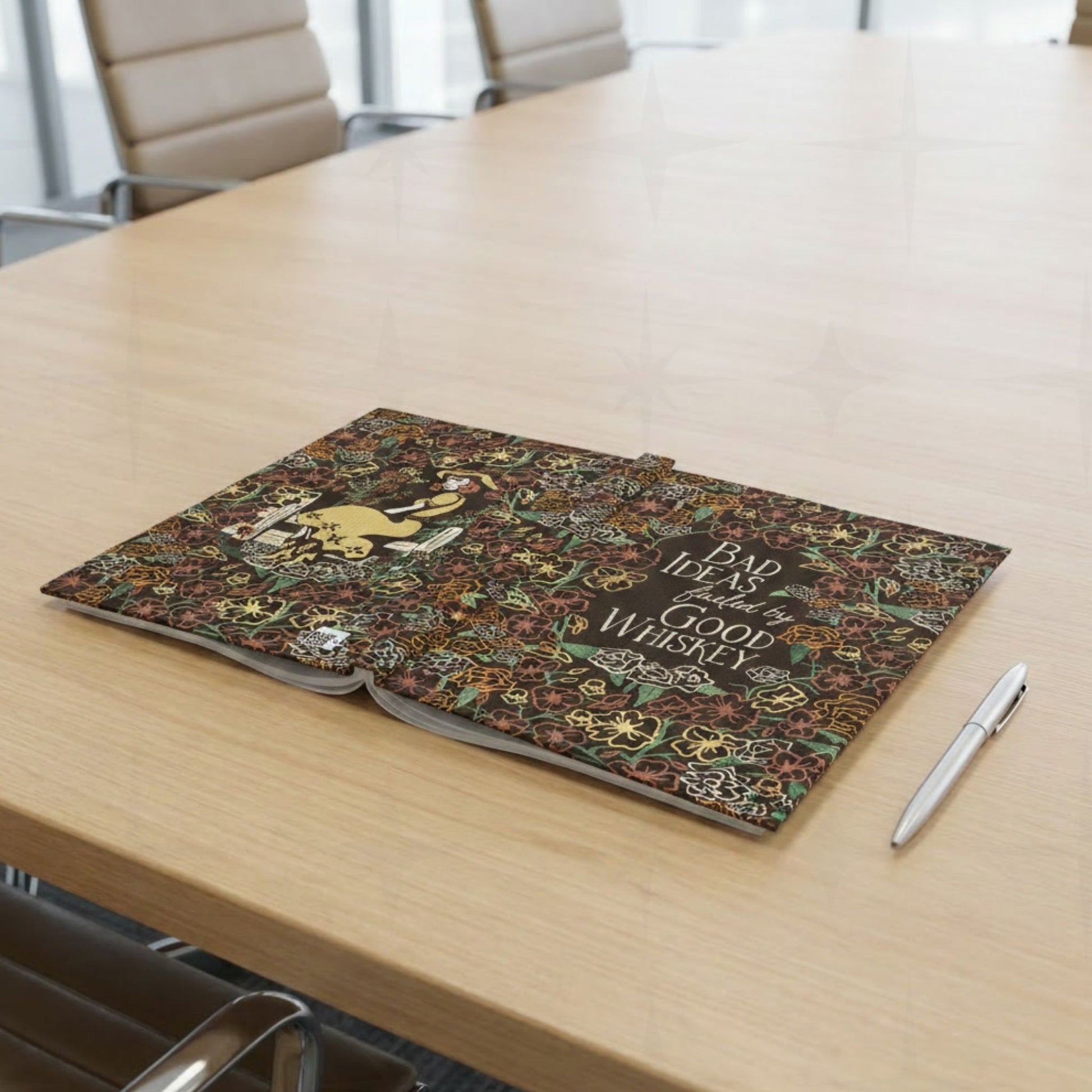 Maximalist floral cowgirl journal open flat on wooden conference table showing full wrap cover design with pen beside it