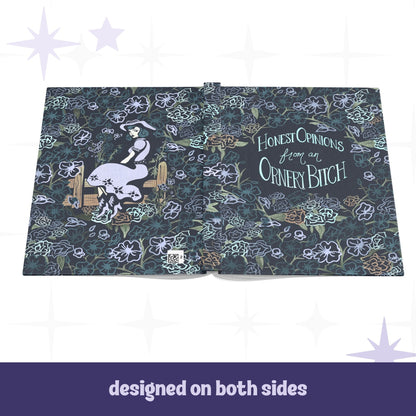Ornery Bitch hardcover journal open flat showing full wrap design with cowgirl pinup illustration on back cover and hand-lettered text on front, dark floral pattern across both sides
