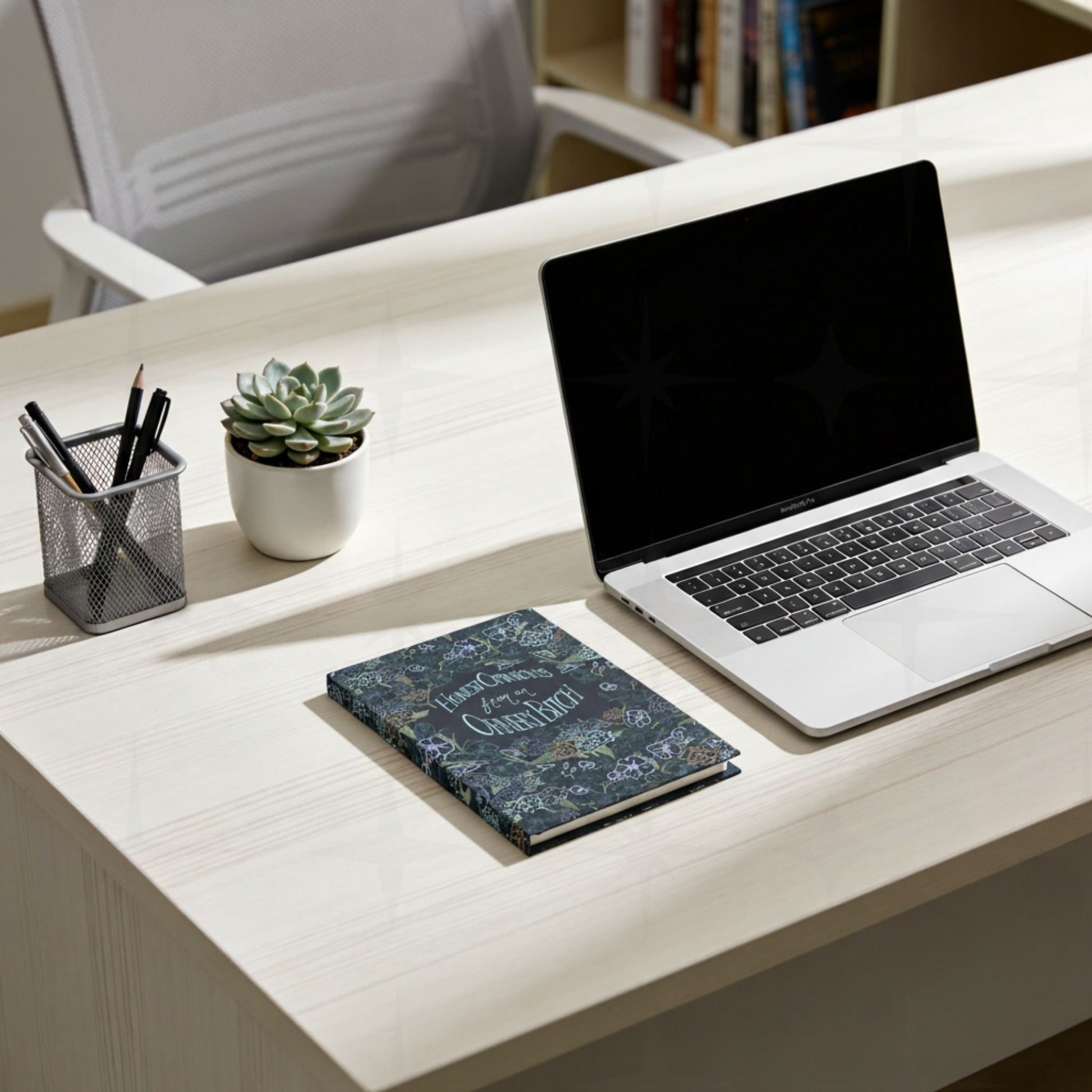 Dark floral ornery bitch hardcover journal on modern office desk next to laptop, pens, and succulent plant in bright workspace