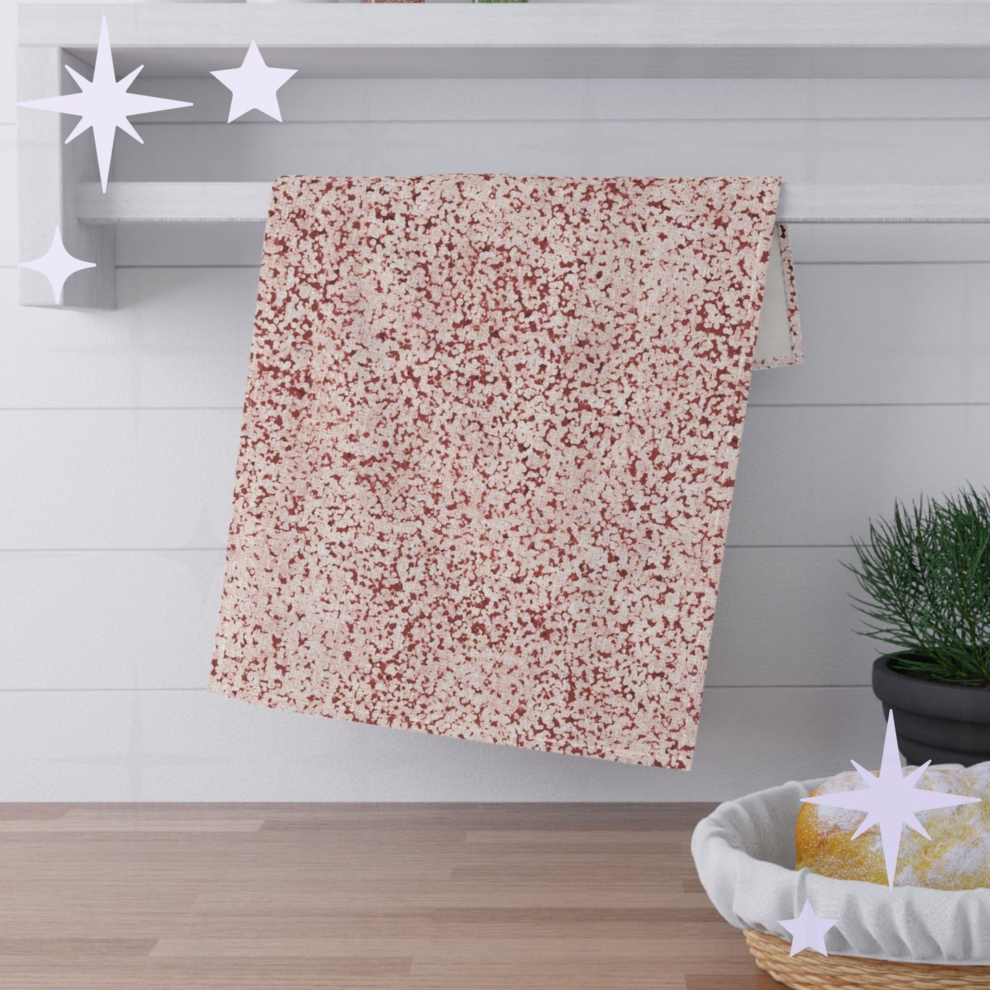 Terracotta red terrazzo tea towel folded and draped over white shaker shelf rail in kitchen setting with pine plant and bread basket