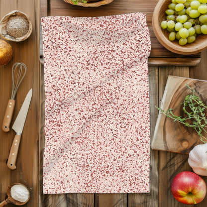 Terracotta red terrazzo print tea towel laid flat on dark wood kitchen prep surface surrounded by cooking props including whisk, knife, grapes, apple, garlic and herbs
