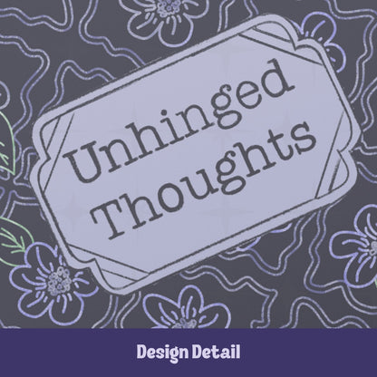 Close-up of hand-lettered Unhinged Thoughts text inside vintage cartouche label on dark floral journal cover showing chalky letterforms and lavender botanical pattern