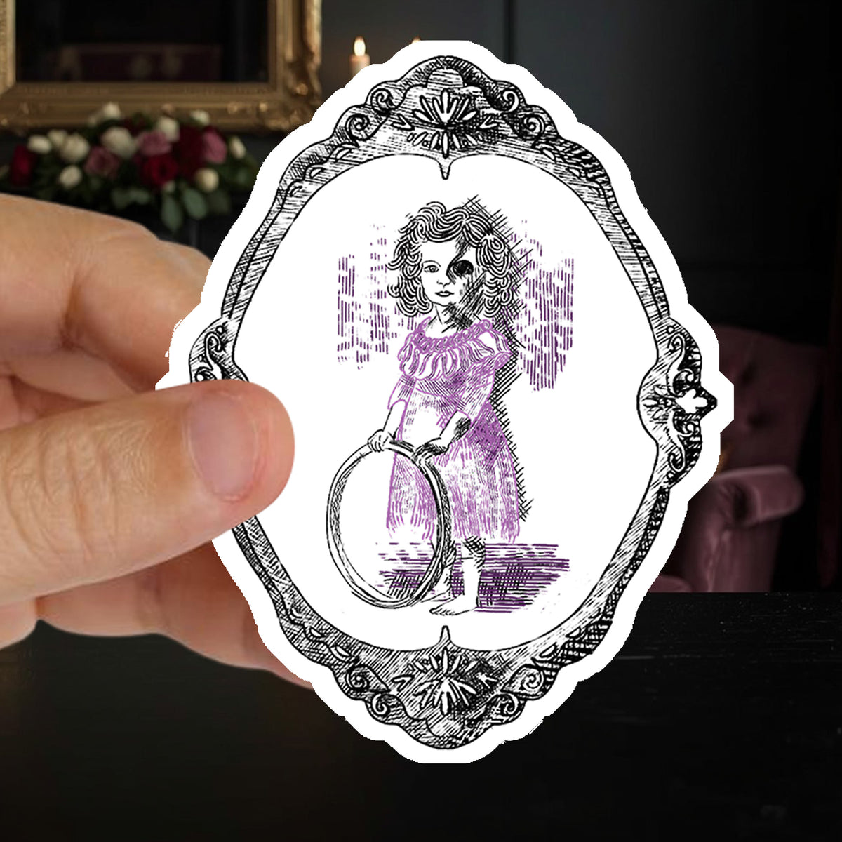 Hand holding a victorian gothic sticker of an undead girl with a hoop in a candlelit parlor