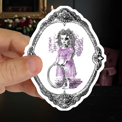 Hand holding a victorian gothic sticker of an undead girl with a hoop in a candlelit parlor